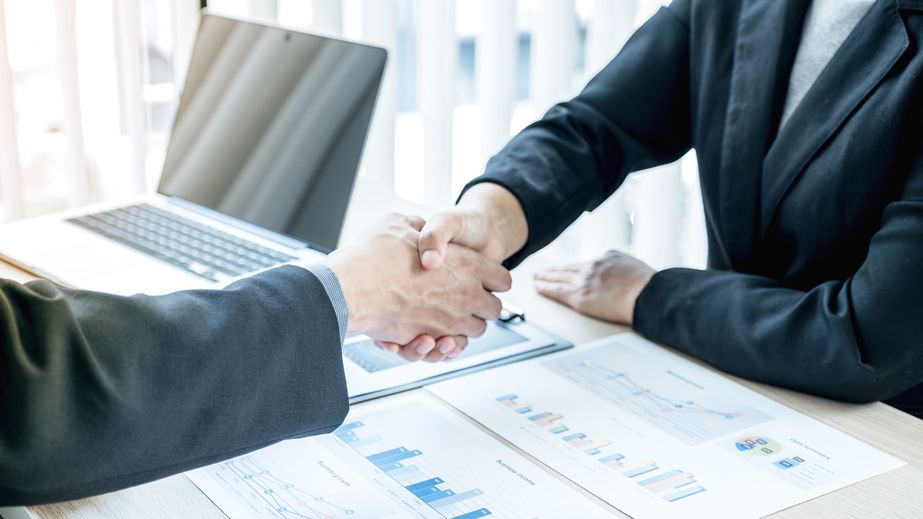 two people shaking hands over a desk full of paperwork